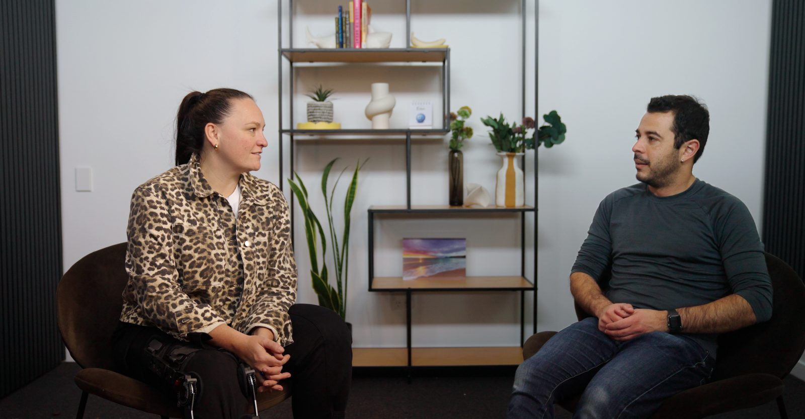 Mel and Pablo sitting facing each other in a studio, mid-conversation.